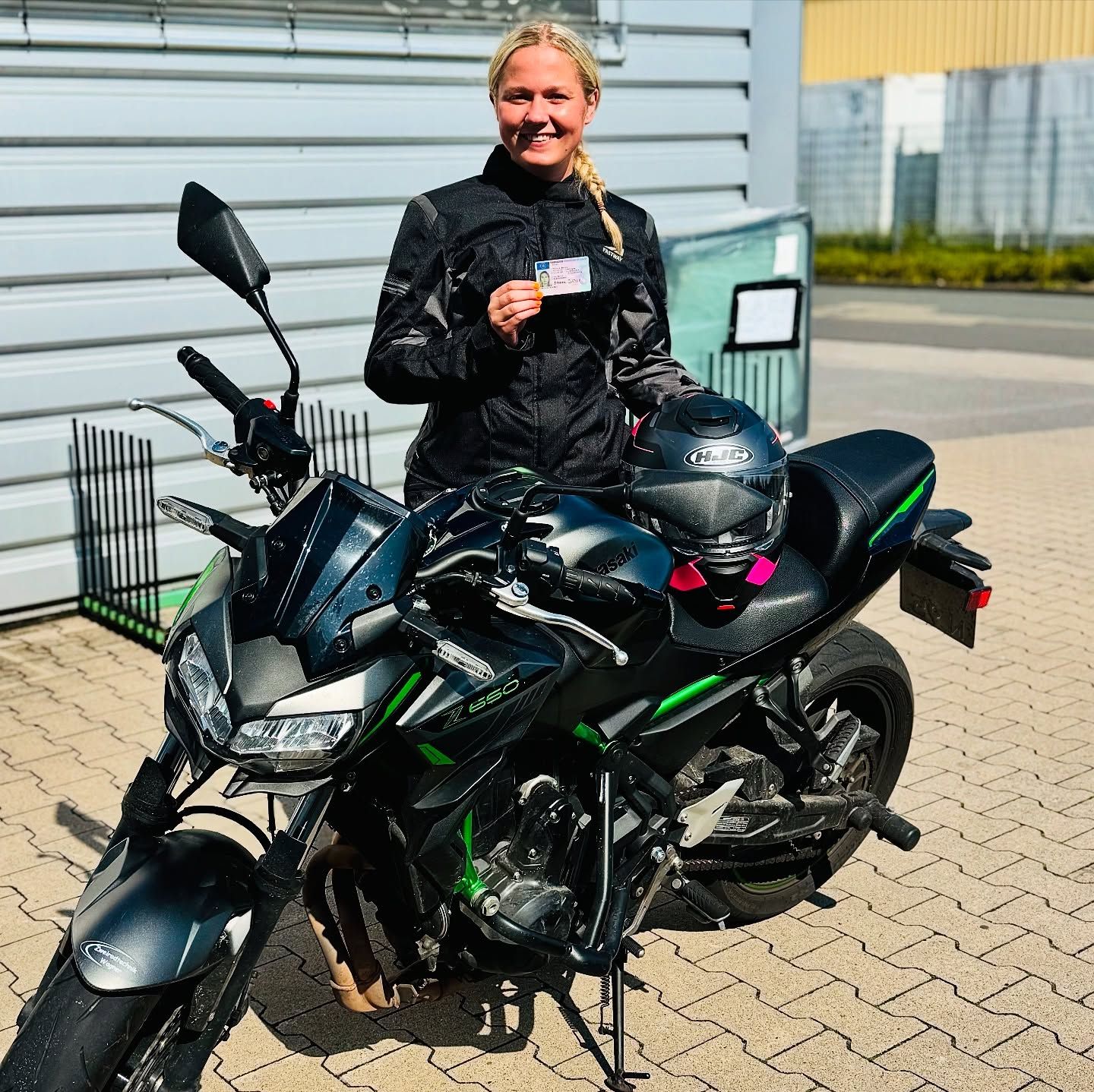 Eine Fahrschülerin mit Prüfungsbescheinigung neben dem Motorrad der Fahrschule